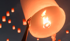Hands releasing a glowing sky lantern into the evening sky, surrounded by other lanterns floating gently upward